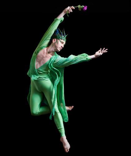 Dancer in a green costume suspended in motion against black